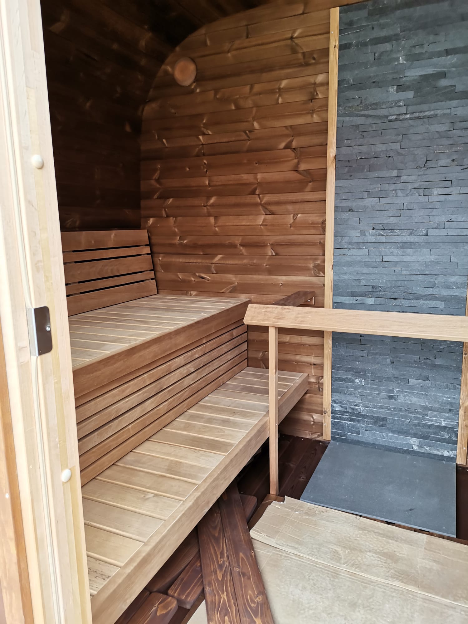 Sauna Exterior Cubus em madeira e pedra com bancos internos.