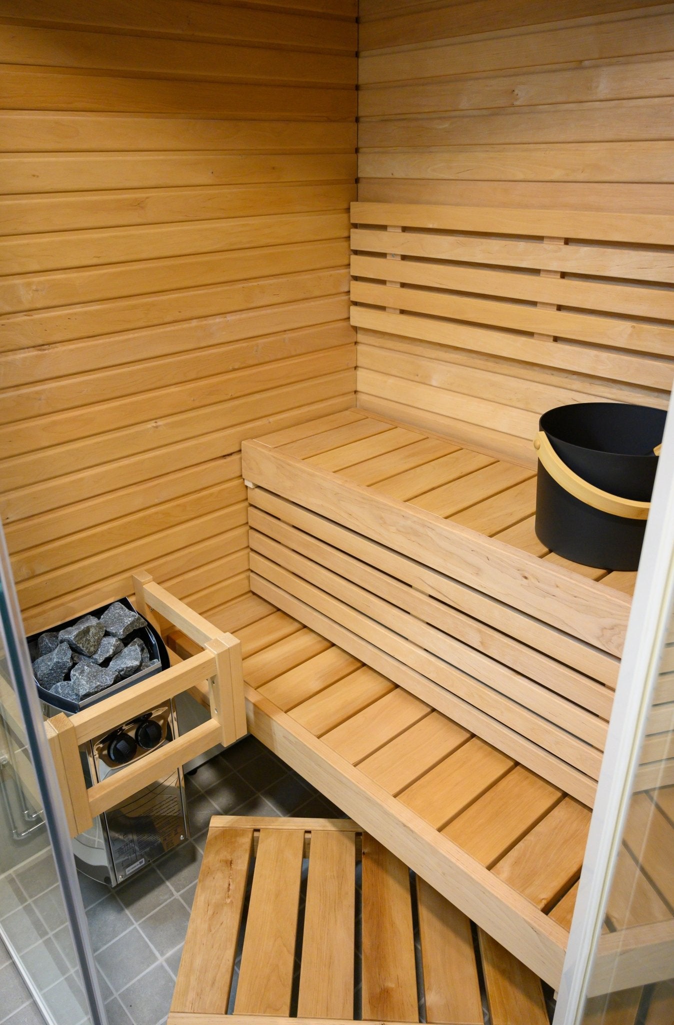 Sauna Sirius Corner com balde e pedras visíveis.