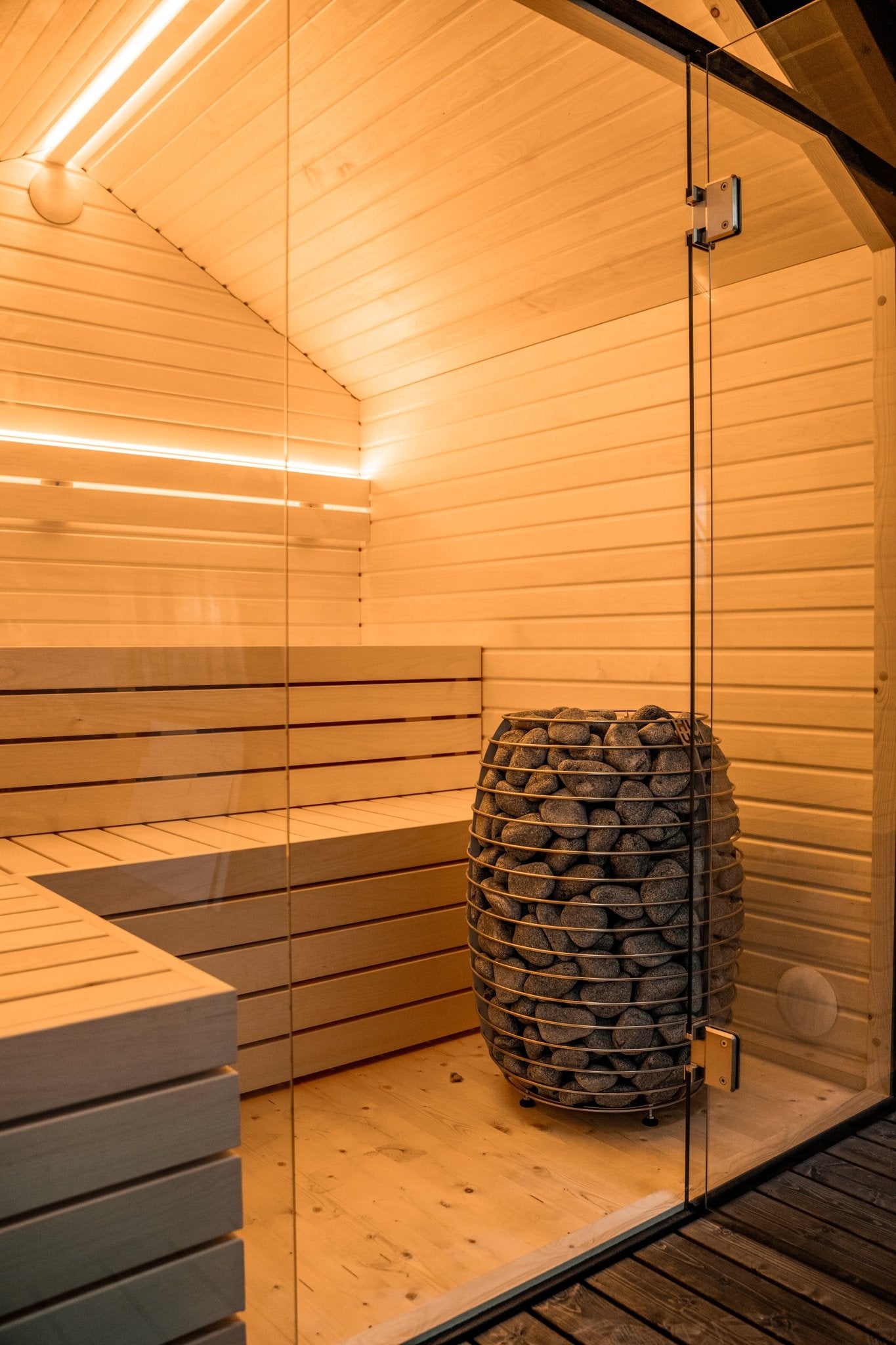 Sauna Exterior Lumi com porta de vidro e pedras visíveis.