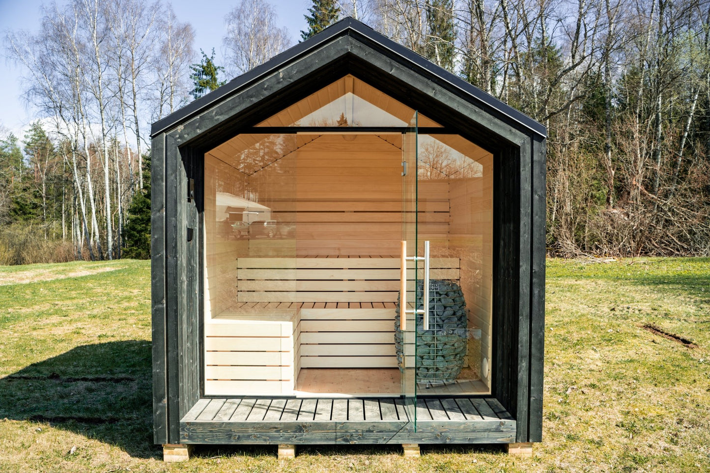 Sauna Exterior Lumi isolada com porta de vidro em área gramada.